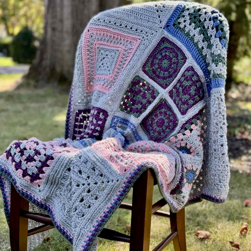 Friendship Blanket hanging from ladder in shades of purple, red, white, and pink by www.suflowercottagecrochet.com