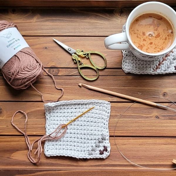 Crochet materials on wooden table crocheting a coaster. Elements Tunisian Crochet Placemat Pattern by Noor’s Knits