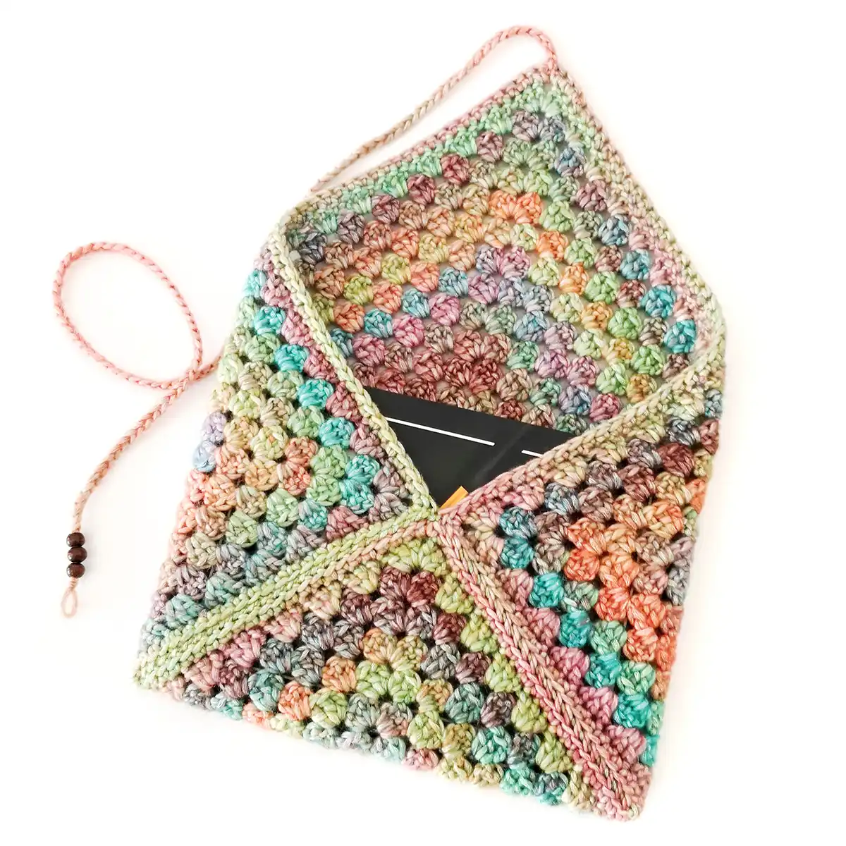 A multicolored granny square crochet book sleeve with a black book inside